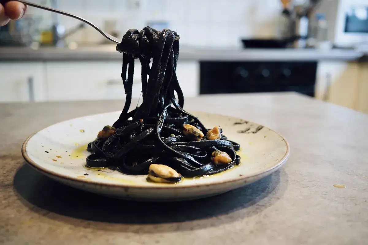 Pâtes noires, colorées avec de l'encre de seiche, c'est quoi ce plat savoureux ? Elles sont servies avec des moules sur une assiette.
