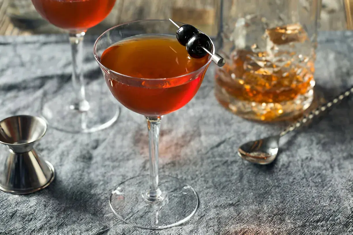Cocktail au whisky garni de cerises, servi avec un verre de whisky et un jigger. Le whisky est-il bon pour les artères ? Une question à méditer.