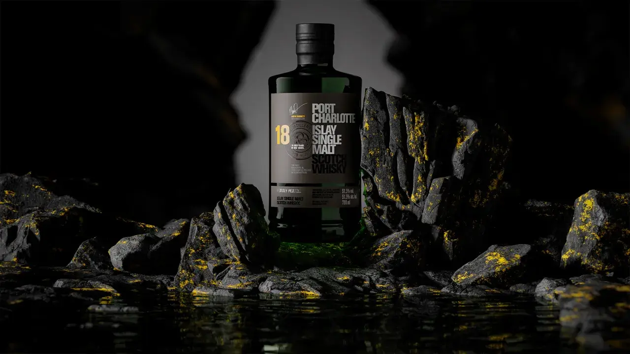 Bouteille de whisky Port Charlotte 18 ans d'âge, produit par la distillerie Bruichladdich, posée sur des rochers sombres aux reflets dorés.