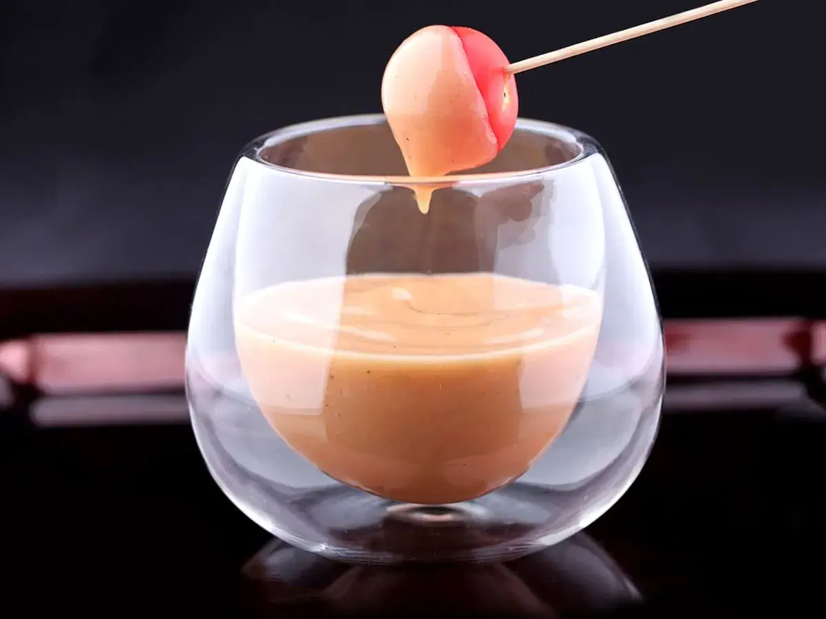 Une tomate cerise trempée dans une sauce cocktail onctueuse, servie dans un verre élégant.
