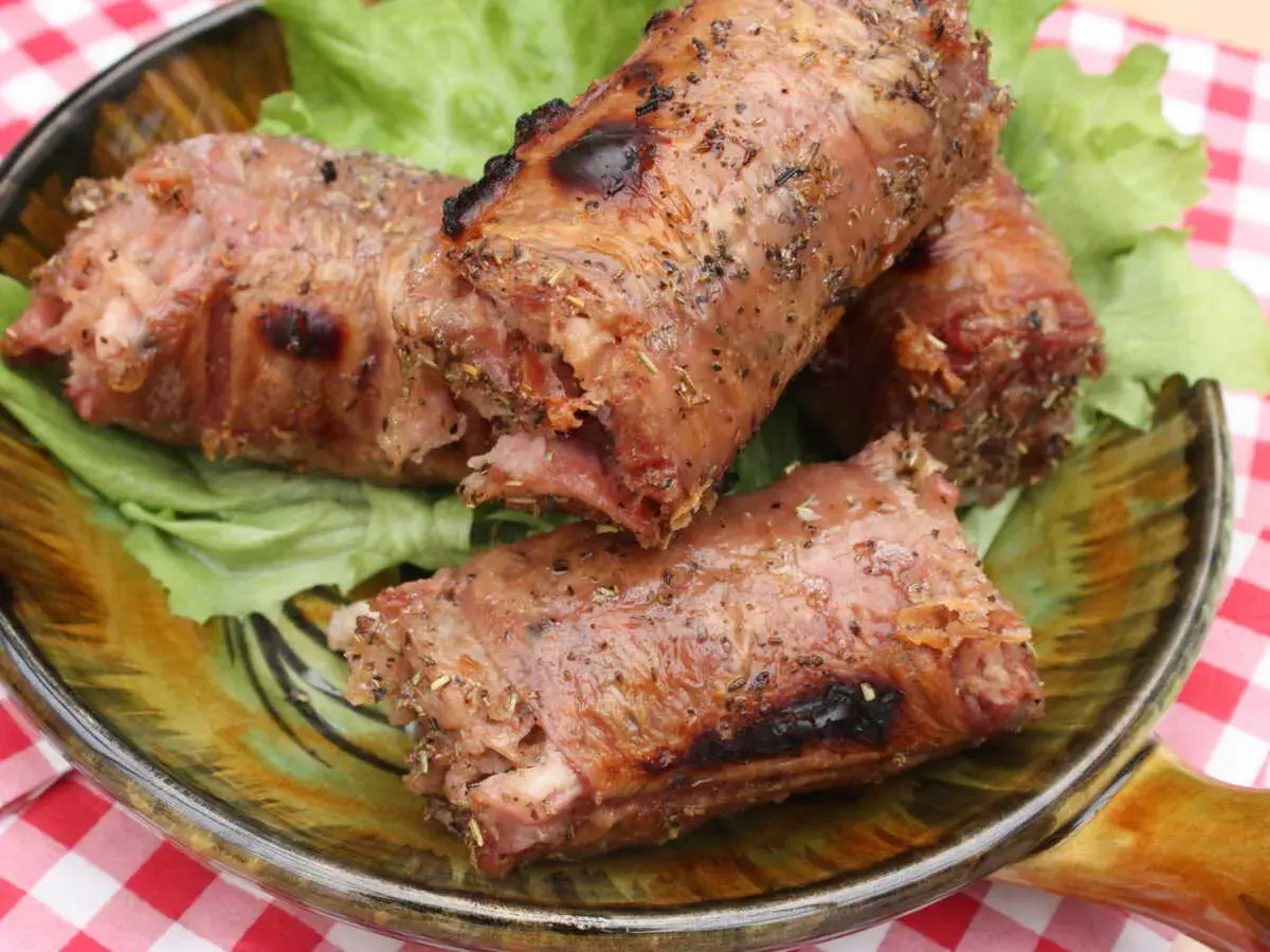 Trois andouillettes grillées au barbecue, servies sur un lit de laitue dans une assiette décorative.