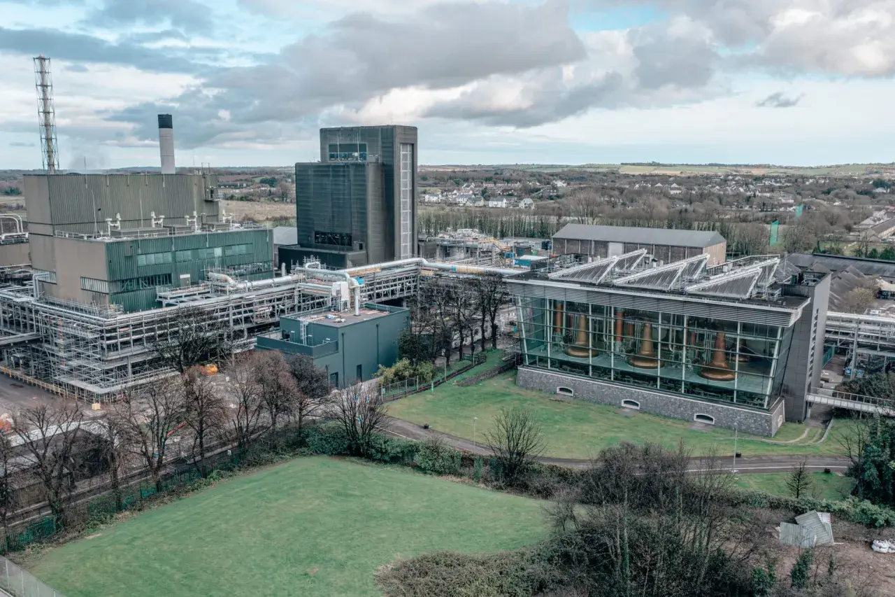 Vue aérienne de la distillerie Midleton, avec ses bâtiments industriels, ses cuves en cuivre visibles à travers une façade vitrée, et un paysage verdoyant en arrière-plan.