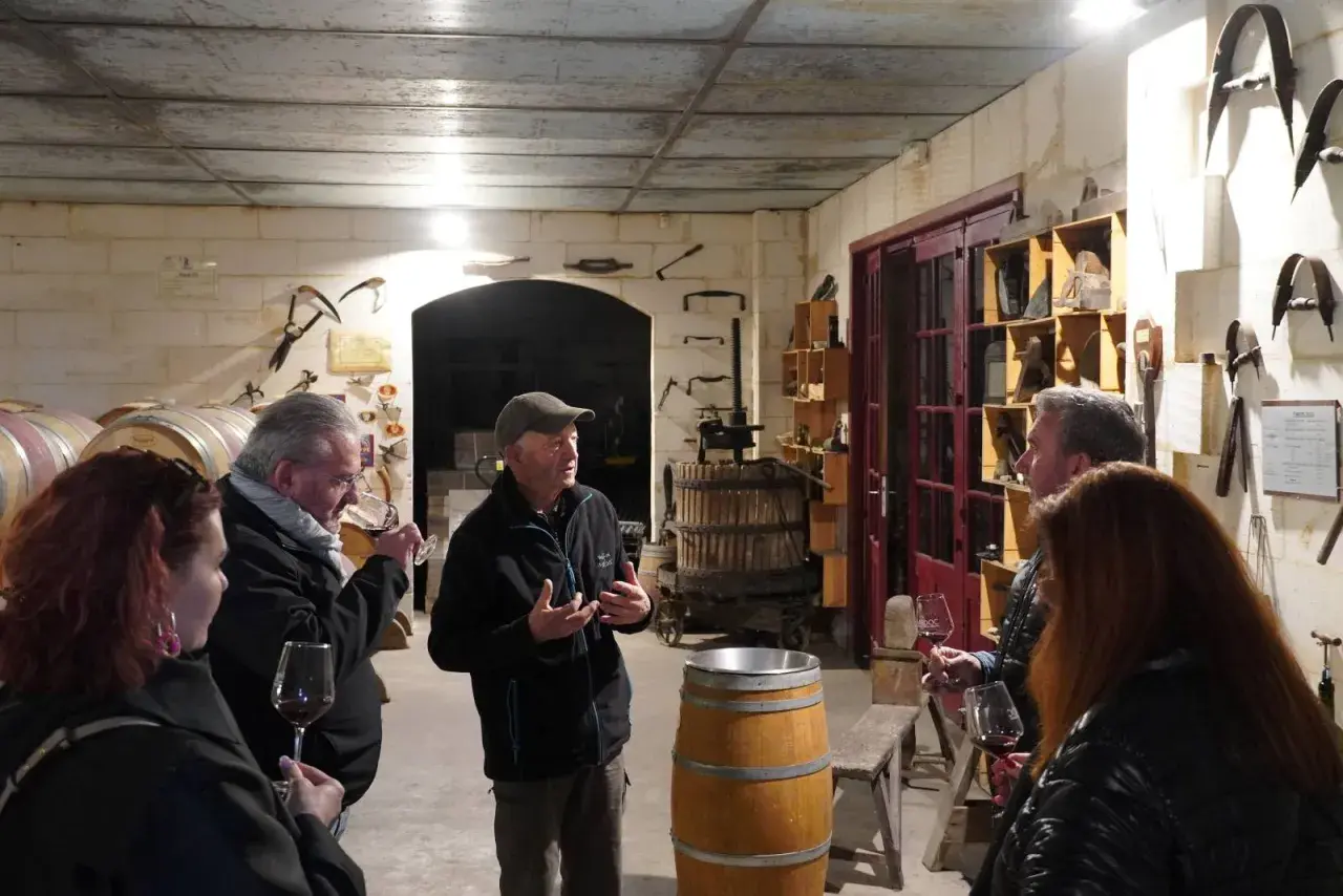 Visite d'une cave à vin du Médoc. Un guide explique la fabrication du vin à des visiteurs, entourés de fûts et d'outils anciens.