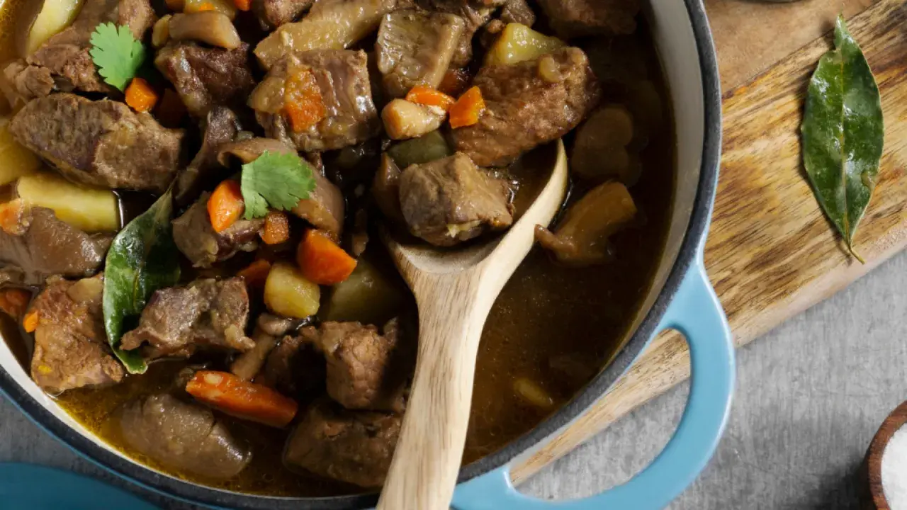 Un savoureux navarin d'agneau, aux carottes et pommes de terre, mijote dans une cocotte bleue. Son origine est un délice.