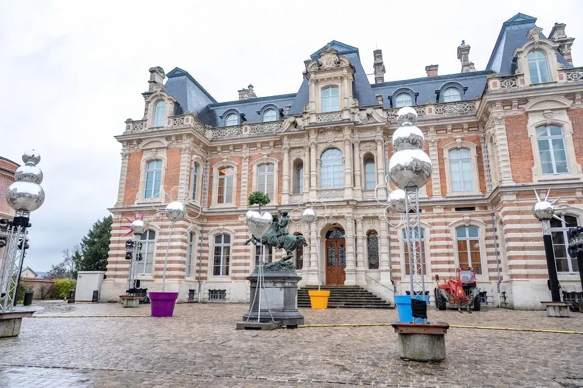 Devant un château, des sphères argentées, comme des habits de lumière, scintillent sur des structures métalliques, entourant une statue équestre.