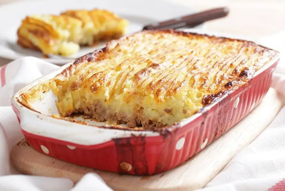 Un plat de hachis parmentier, dont l'origine remonte à Antoine-Augustin Parmentier, est servi dans un plat rouge à pois blancs.