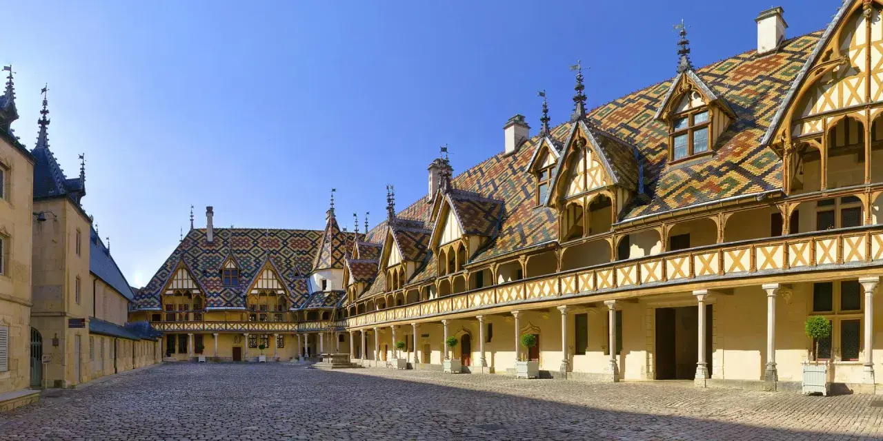 Cour intérieure des Hospices de Beaune, un joyau architectural à visiter. Toits colorés, arcades et pavés de pierre.