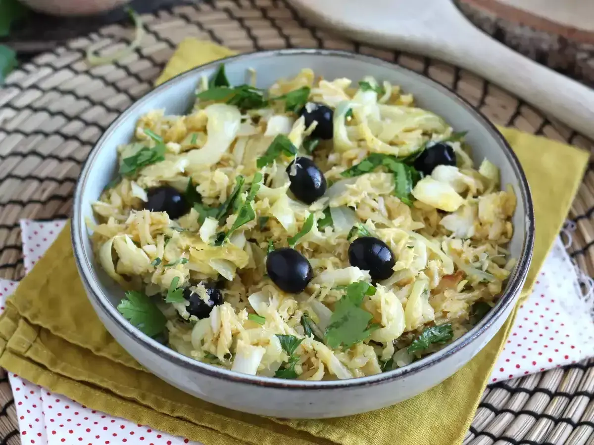 Un plat de bacalhau à brás, effiloché et mélangé avec des pommes de terre, des oignons et des olives noires, garni de persil frais.