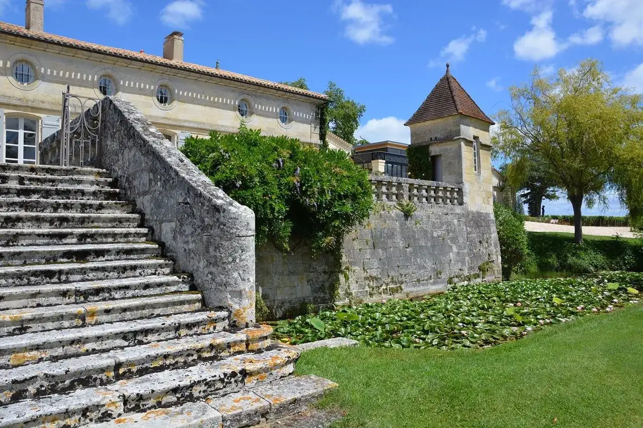 Escalier de pierre menant à un château, avec un étang de nénuphars. Une belle journée pour une visite château Pomerol.
