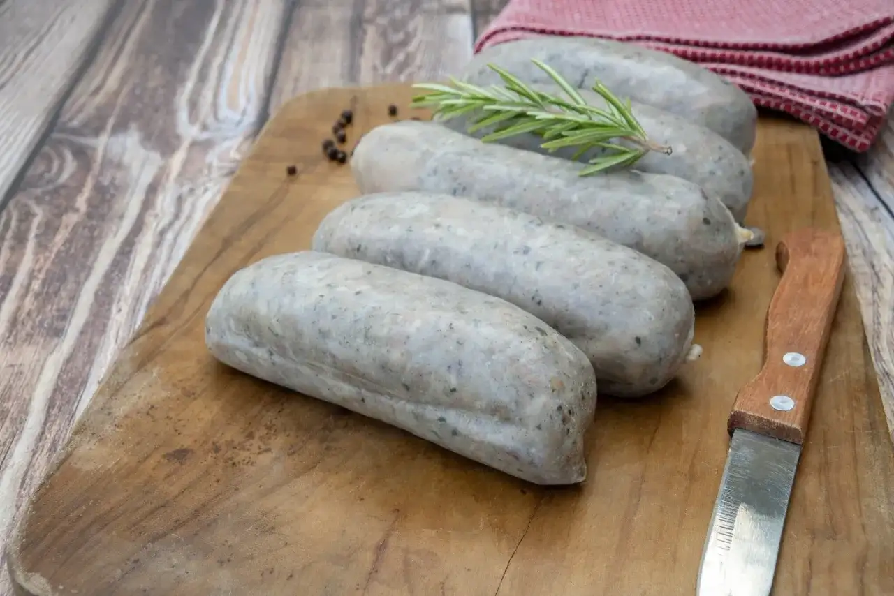 Saucisses grises sur planche en bois, avec romarin et poivre. La différence entre andouille et andouillette est subtile, mais la texture ici suggère une andouillette.