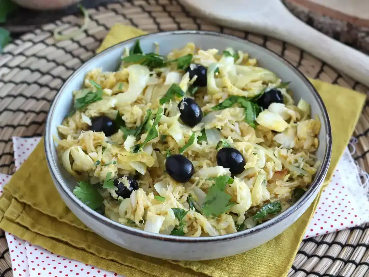 Un plat de bacalhau à brás, effiloché et mélangé avec des pommes de terre, des oignons et des olives noires, garni de persil frais.