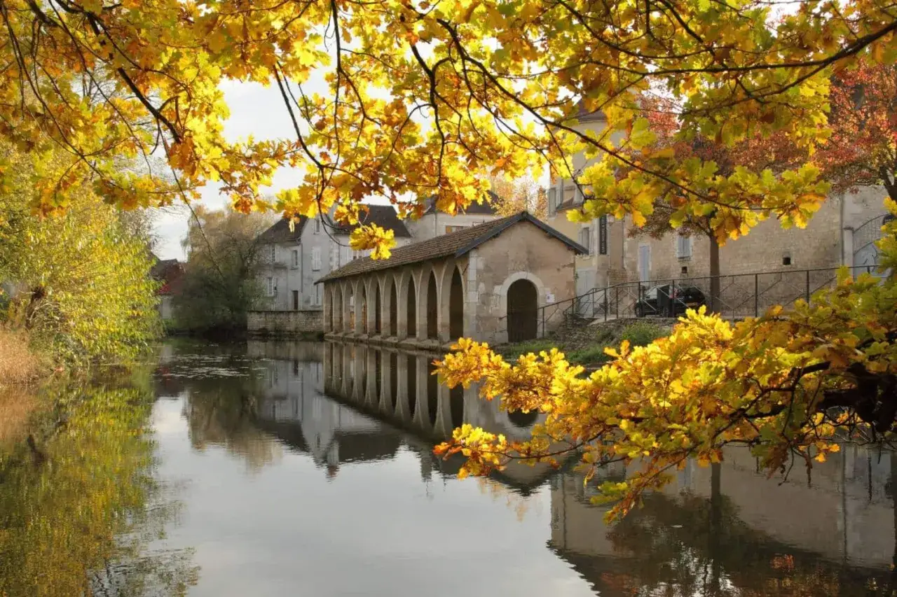 Bord de rivi&egrave;re &agrave; Chablis ville, reflets dor&eacute;s des feuilles d'automne sur l'eau calme, un lavoir ancien bord&eacute; d'arches.