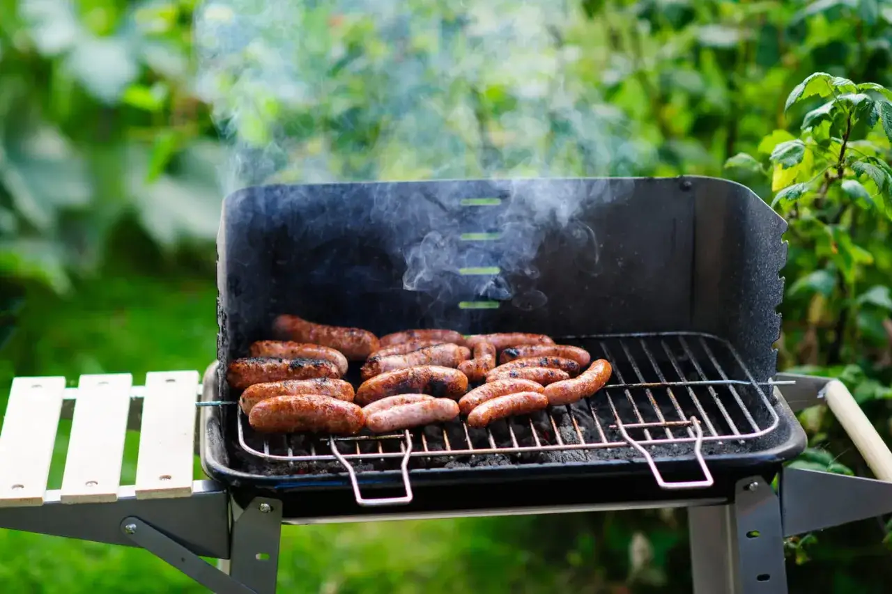 Des chipolatas grillées, fumantes et dorées, évoquant l'origine d'un bon barbecue estival.