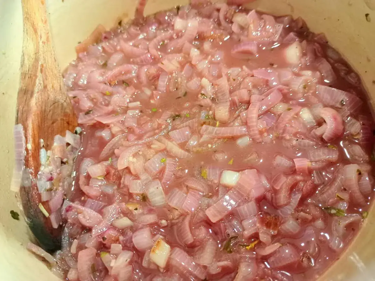 Cuill&egrave;re en bois remuant des oignons rouges mijot&eacute;s dans une sauce au vin blanc pour viande.