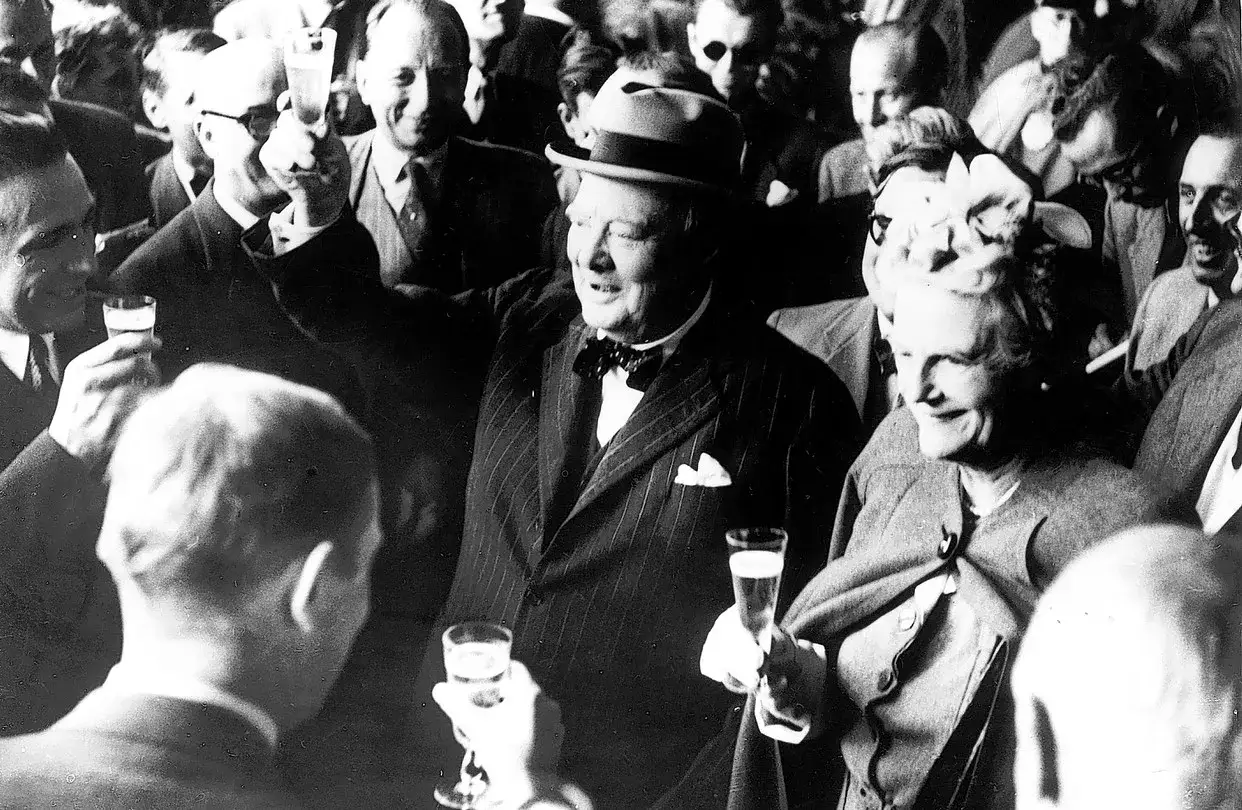 Churchill, chapeau sur la tête, lève son verre. Une foule joyeuse l'entoure, célébrant avec du churchill alcool.