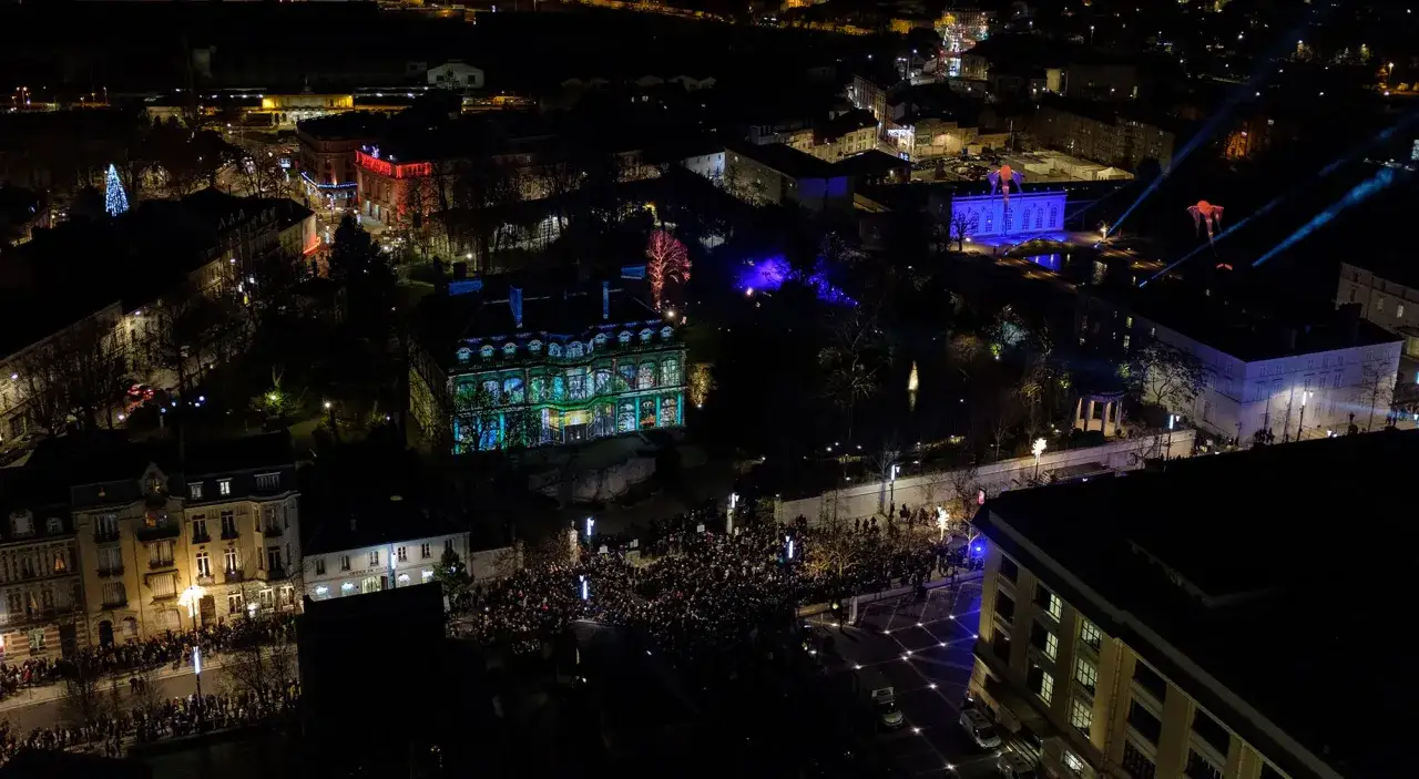 Une foule admire un spectacle de projection lumineuse sur un bâtiment, une scène féerique où les habits de lumière transforment la nuit en un tableau vivant.