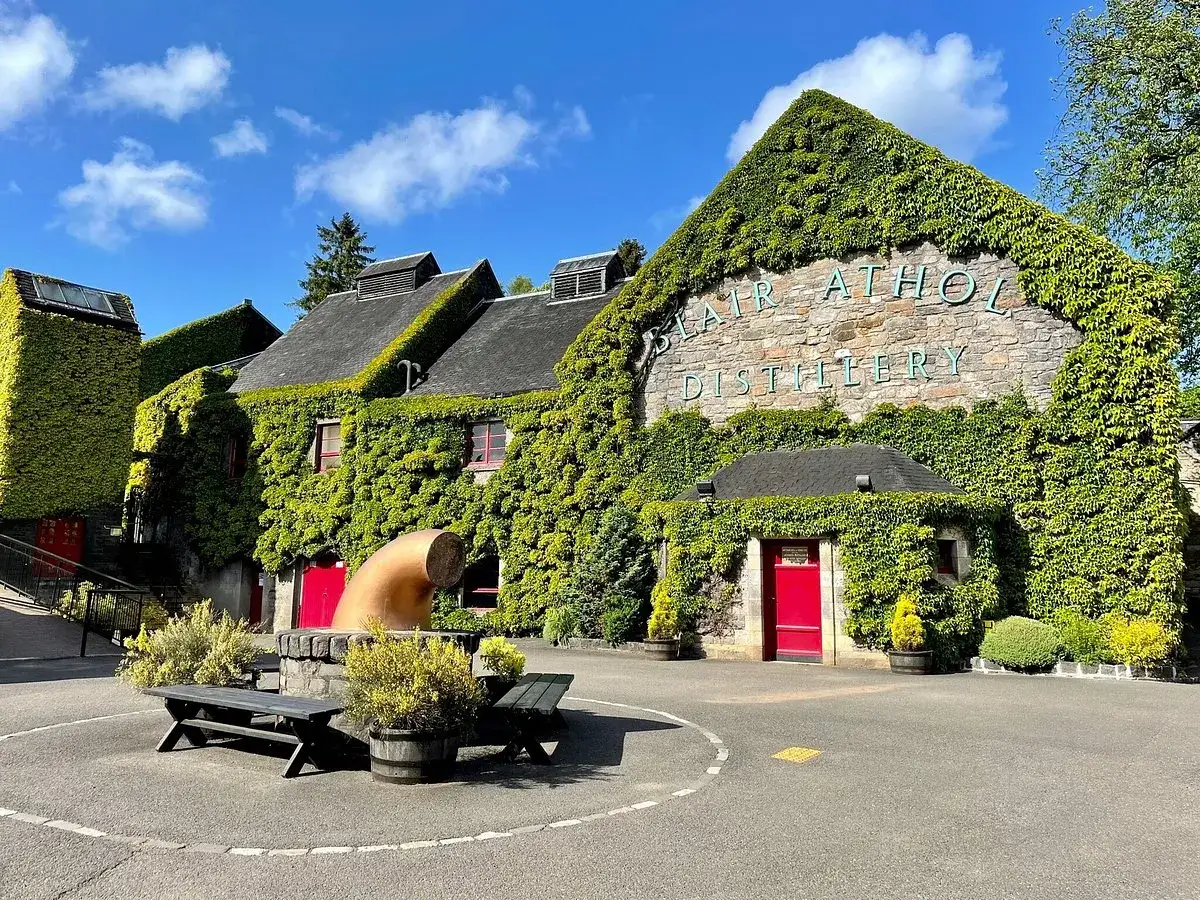 La distillerie Blair Athol, recouverte de verdure, invite à découvrir ses secrets. Un lieu historique sous un ciel bleu.
