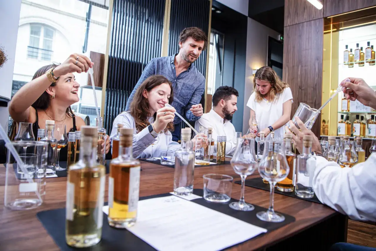 Des participants joyeux lors d'un cours dégustation whisky, manipulant pipettes et verres.
