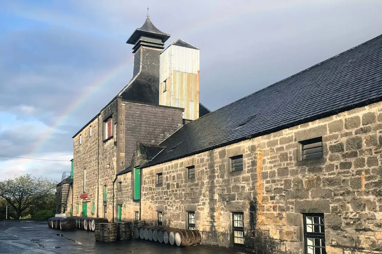 Un arc-en-ciel appara&icirc;t au-dessus de la distillerie Benriach, avec des tonneaux de whisky align&eacute;s devant les b&acirc;timents en pierre.
