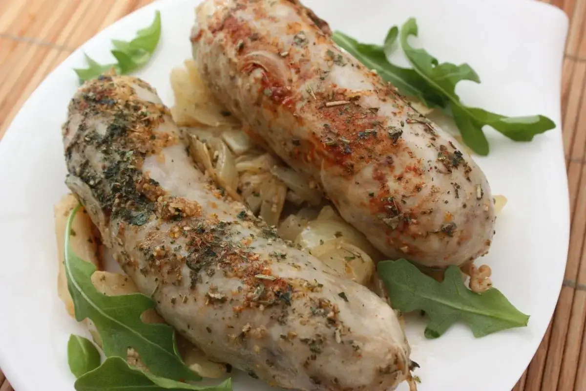 Deux andouillettes savoureuses, garnies d'herbes et d'épices, reposent sur un lit d'oignons caramélisés et de roquette fraîche.