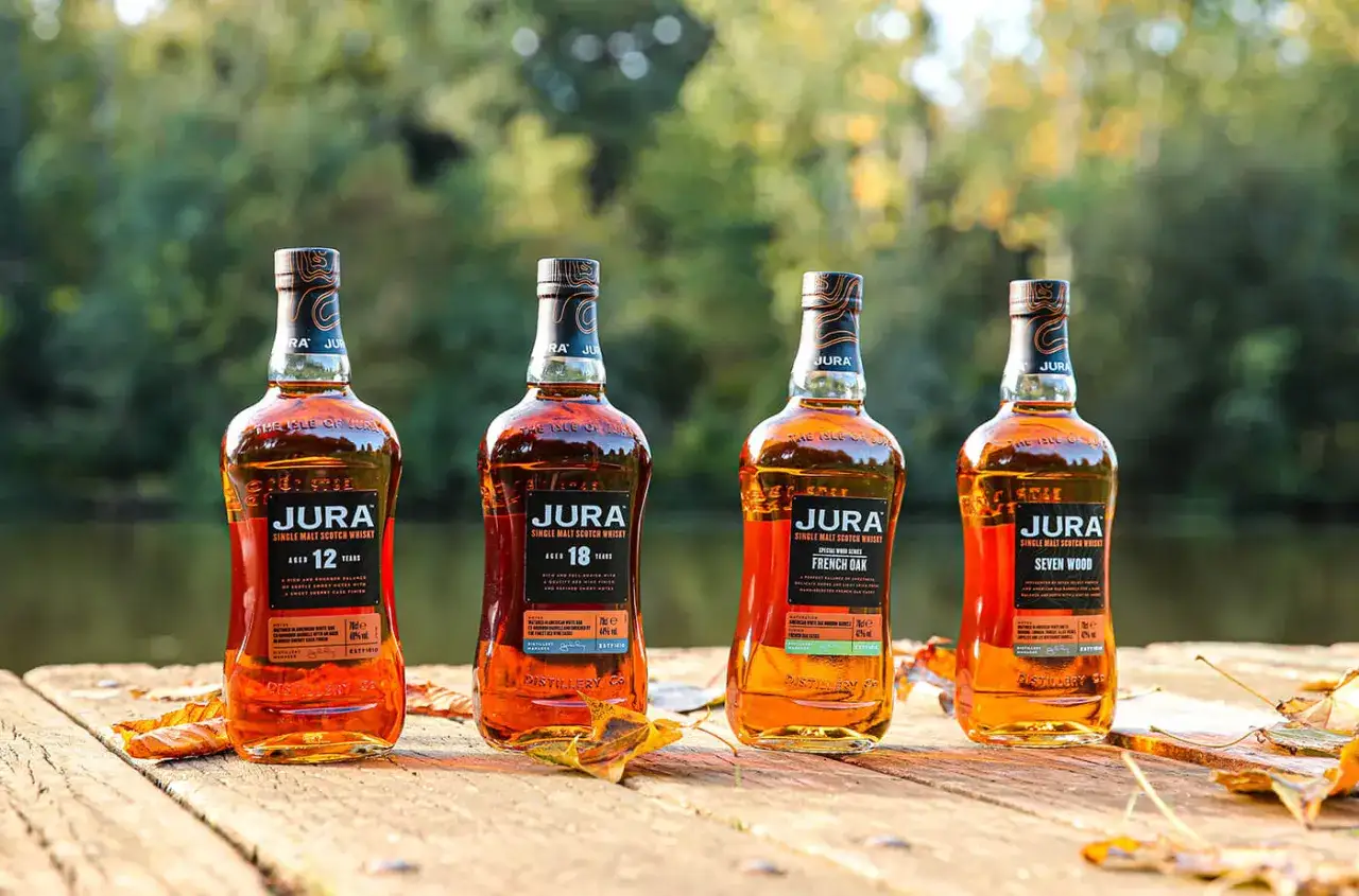Quatre bouteilles de whisky Jura Single Malt Scotch, dont un 12 ans, un 18 ans, un French Oak et un Seven Wood, sur une table en bois. Avis sur le whisky Jura.