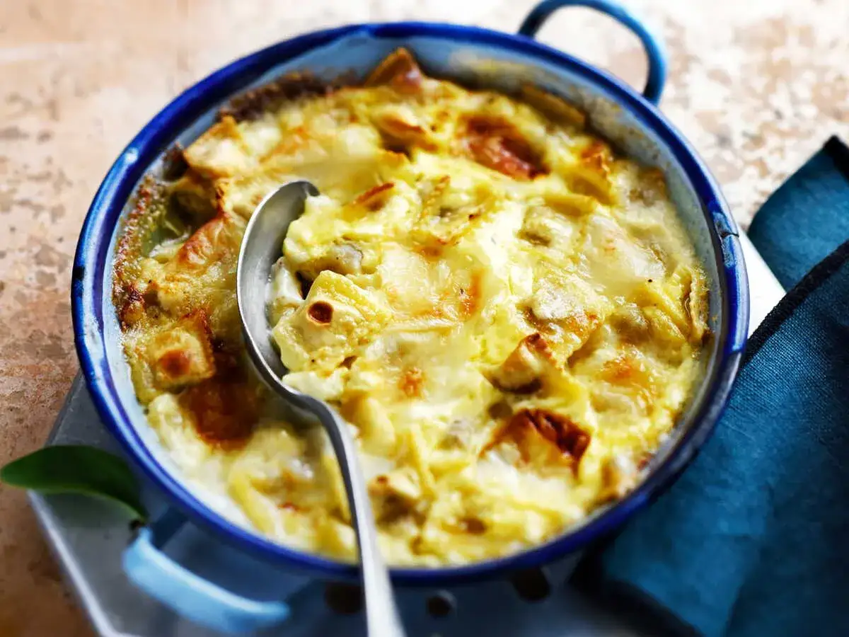 Un plat de ravioli du Dauphiné gratiné, prêt à être dégusté. Une cuillère en argent est posée sur le plat bleu émaillé.