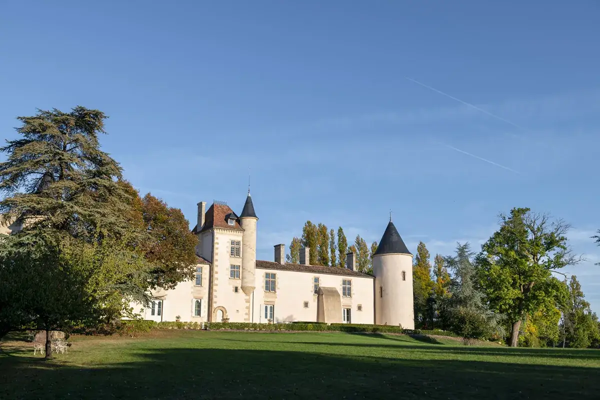Le ch&acirc;teau de Toulouse-Lautrec, un &eacute;difice de pierre claire avec des tours coniques, se dresse sous un ciel bleu clair, entour&eacute; d'arbres aux couleurs d'automne.