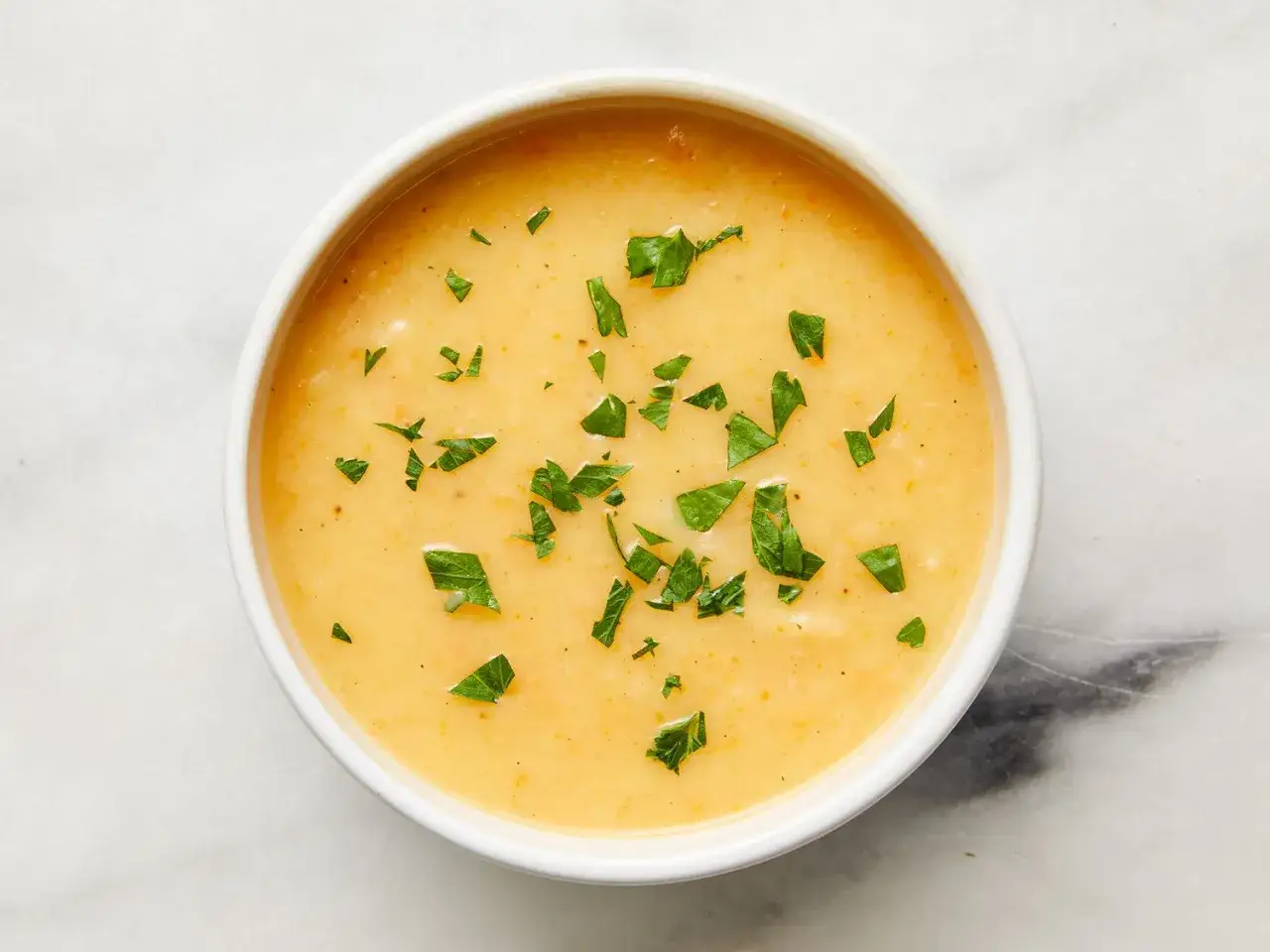Un bol de potage Dubarry crémeux, garni de persil frais, sur fond marbré.