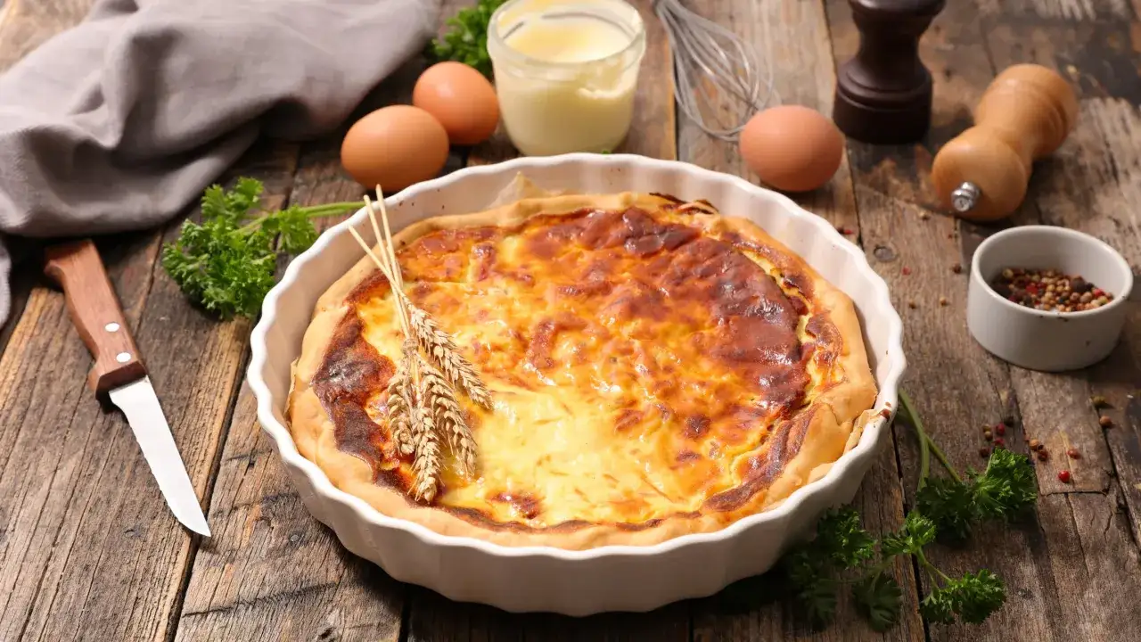 Une quiche lorraine gourmande, dorée et appétissante, sur une table en bois rustique. Des épis de blé ajoutent une touche champêtre.