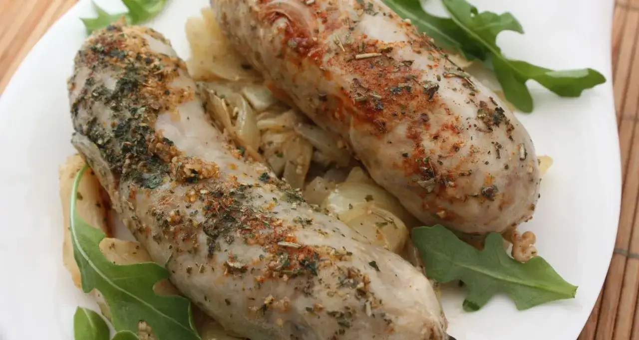 Deux andouillettes savoureuses, assaisonnées d'herbes et d'épices, prêtes pour la cuisson, servies sur un lit d'oignons et de roquette.