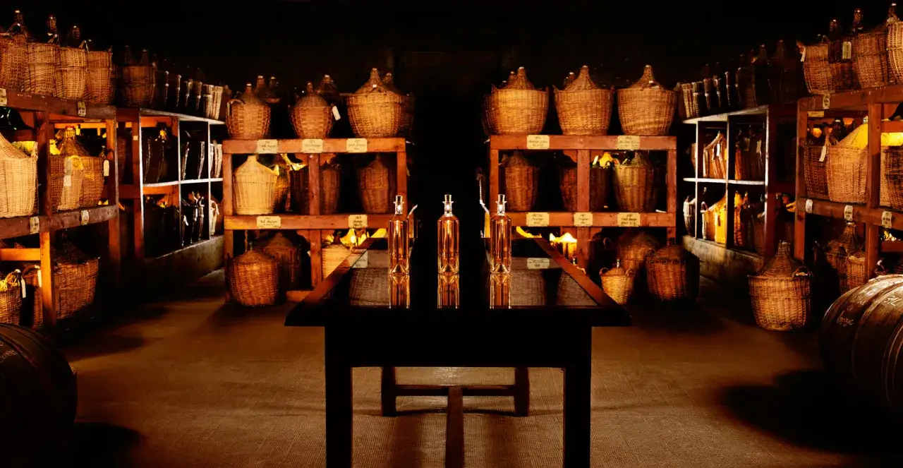 Cave de vieillissement pour le cognac Martell, remplie de bonbonnes en osier et de bouteilles.