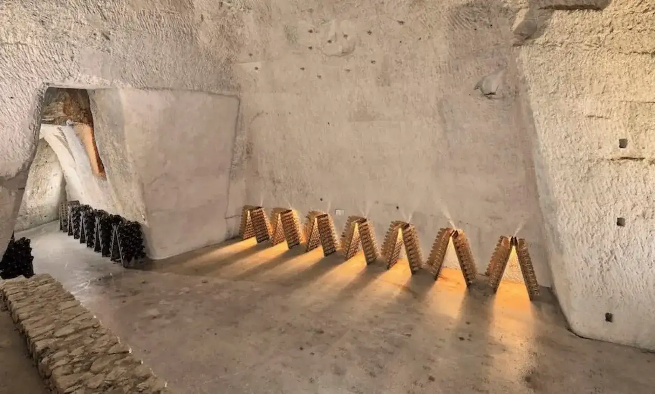 Visite cave champagne : bouteilles en pupitres dans un chai troglodyte éclairé.