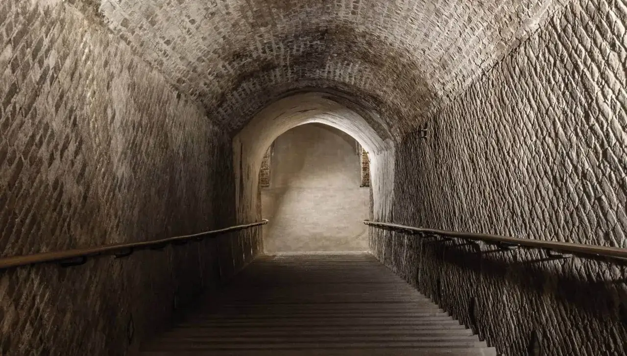 Descente dans les crayères de Ruinart. Un escalier mène à travers un tunnel voûté, offrant un aperçu de l'histoire. Visite cave Ruinart avis.