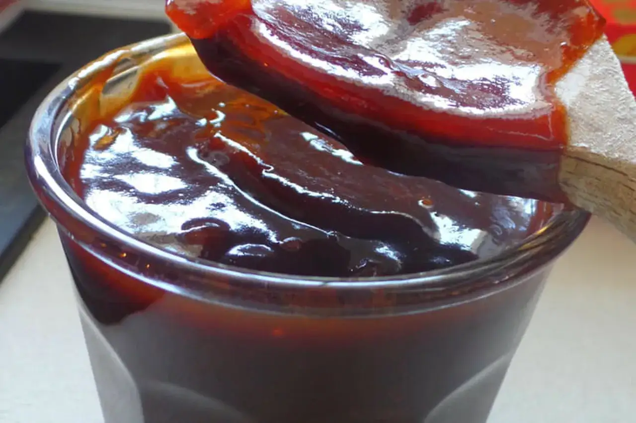Une cuill&egrave;re en bois pr&eacute;l&egrave;ve une sauce barbecue &eacute;paisse et brillante d'un pot en verre. Parfait pour votre prochaine recette de sauce barbecue.