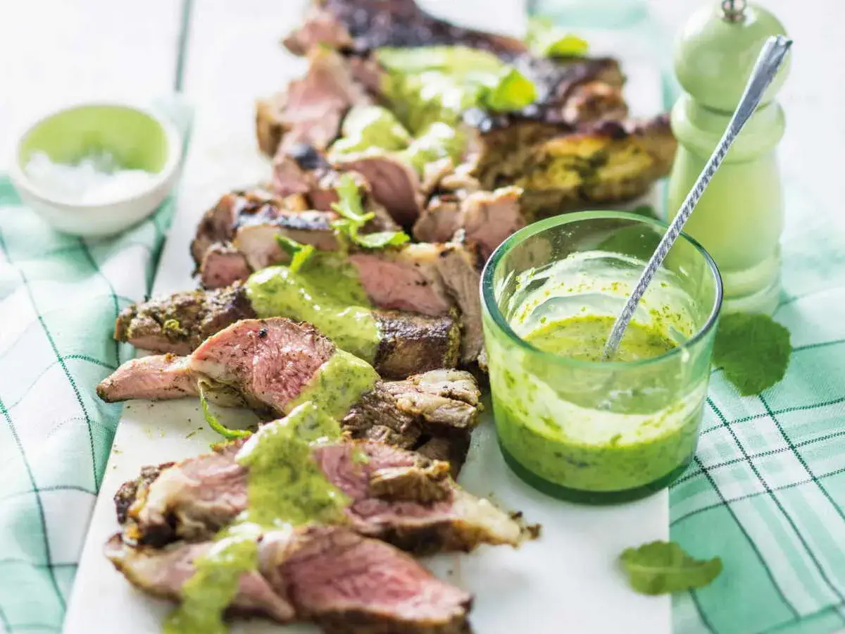 Agneau tranché, arrosé d'une sauce à la menthe fraîche et vibrante, prêt à être dégusté.