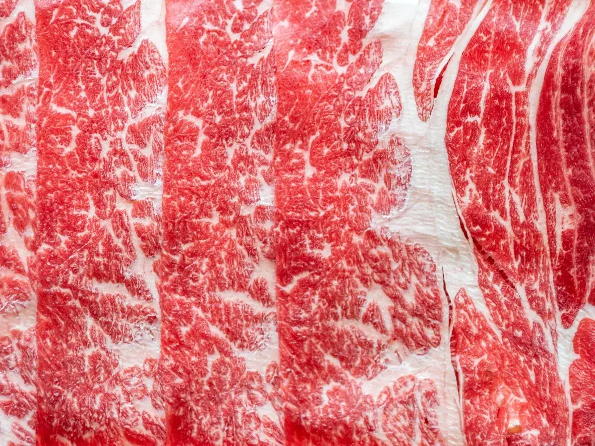 Tranches de bœuf persillé, marbré de gras blanc, promettant le meilleur bœuf du monde. Une texture riche et appétissante.