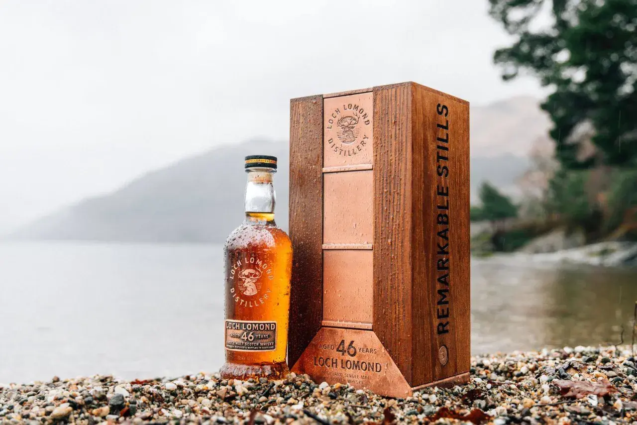 Bouteille de whisky Loch Lomond 46 ans, présentée avec son coffret en bois sur un rivage caillouteux. Un décor qui évoque les aventures du Capitaine Haddock.