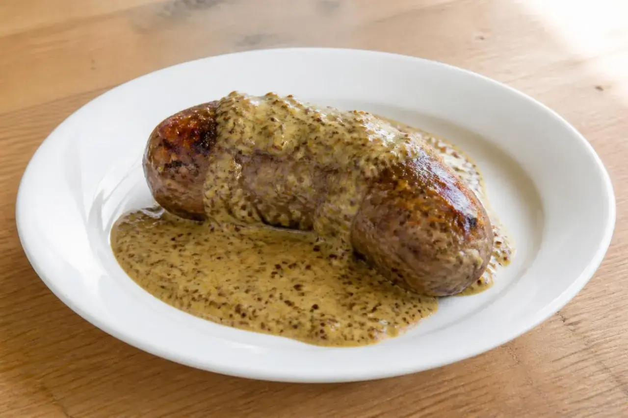 Une andouillette généreusement nappée de sauce moutarde, prête à être dégustée sur une assiette blanche.