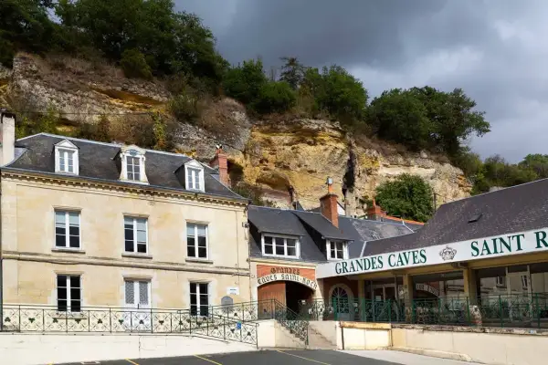 La maison Lacheteau, avec ses façades en pierre et ses toits d'ardoise, se dresse au pied d'une falaise rocheuse.
