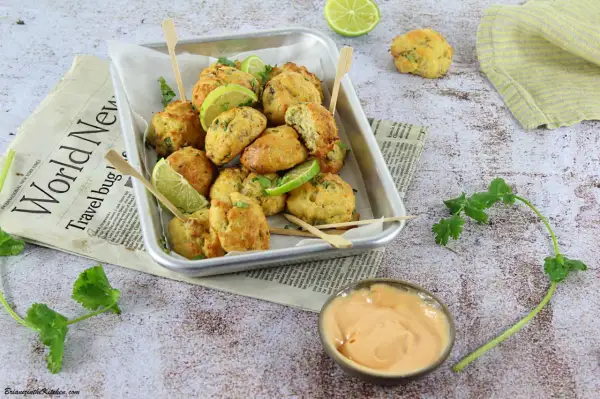 Plateau de délicieux accras dorés, garnis de quartiers de citron vert et de coriandre fraîche, servis avec une sauce crémeuse.