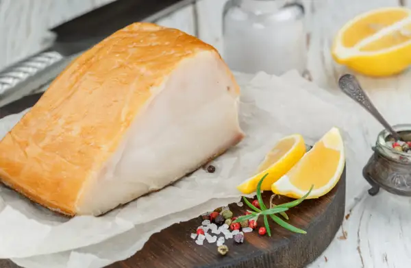Un beau morceau de haddock fumé, prêt pour la cuisson, accompagné de quartiers de citron, de romarin et d'un mélange de poivre et de sel.