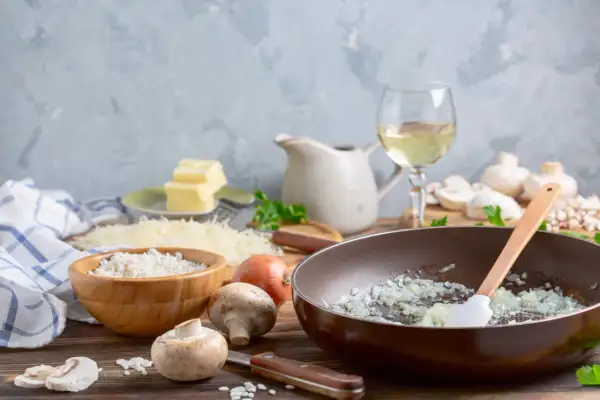 Préparation d'une sauce au vin blanc pour viande : oignons dans une poêle, riz, champignons, beurre, parmesan et vin blanc.