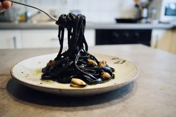 Pâtes noires, colorées avec de l'encre de seiche, c'est quoi ce plat savoureux ? Elles sont servies avec des moules sur une assiette.