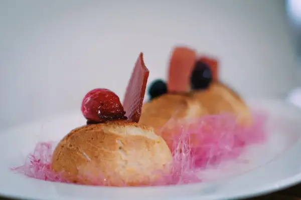 Un ou une profiterole décoré d'une framboise, d'une tuile de chocolat et de barbe à papa rose.