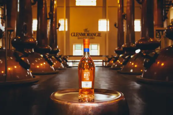 Bouteille de whisky Glenmorangie 18 ans posée sur un plateau en cuivre, au cœur de la distillerie Glenmorangie, entourée d'alambics en cuivre.