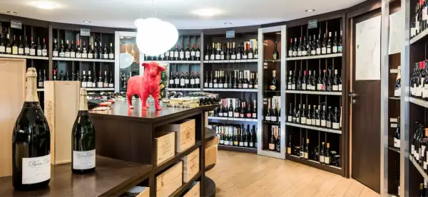 Une cave à vin bien garnie, avec une statue de taureau rouge au centre. Des bouteilles de champagne et de vin sont exposées sur des étagères.
