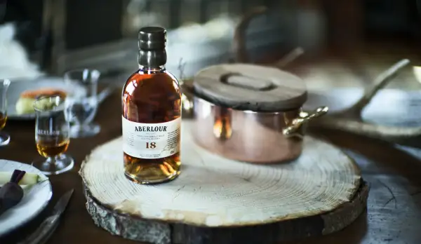 Bouteille d'Aberlour 18 ans, un whisky d'exception, posée sur une tranche de bois. Une expérience de dégustation unique, fruit d'une **création whisky** raffinée.