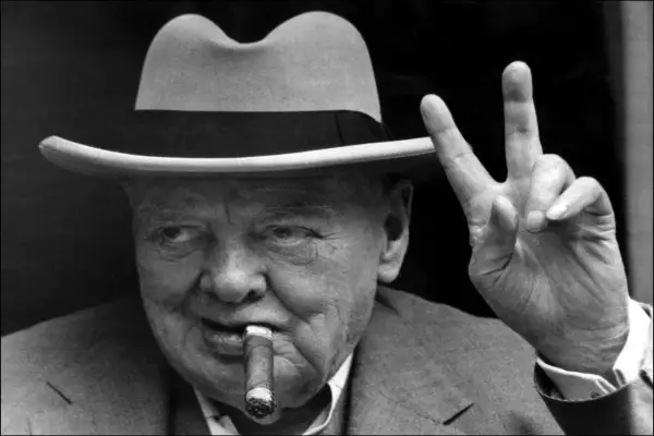 Winston Churchill, chapeau, cigare et signe de victoire. L'alcool et le cigare font partie de son image iconique.