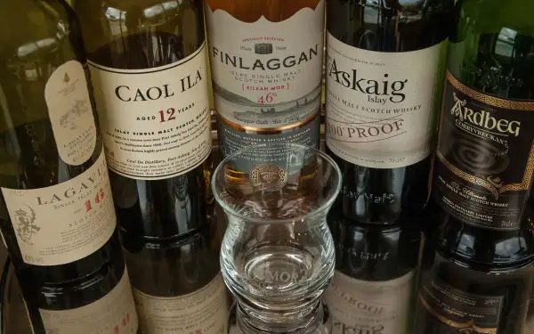 Bouteilles de whisky Islay tourbé : Caol Ila, Lagavulin, Finlaggan, Port Askaig, Ardbeg. Un verre à dégustation vide est au centre.