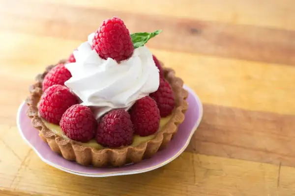 Tartelette garnie de framboises fraîches et d'une délicate crème chantilly, évoquant l'origine d'une douceur intemporelle.